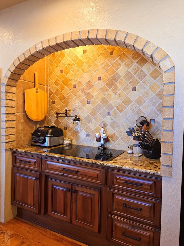 bar featuring light wood finished floors, backsplash, and black electric cooktop