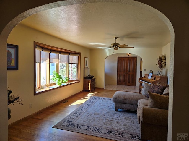 living area with light wood-style floors, arched walkways, a textured ceiling, and baseboards