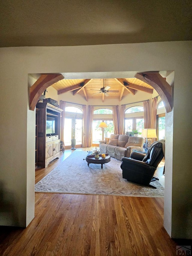 living area with arched walkways, vaulted ceiling with beams, ceiling fan, wood finished floors, and wooden ceiling