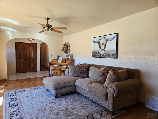 living room with arched walkways, ceiling fan, wood finished floors, and visible vents