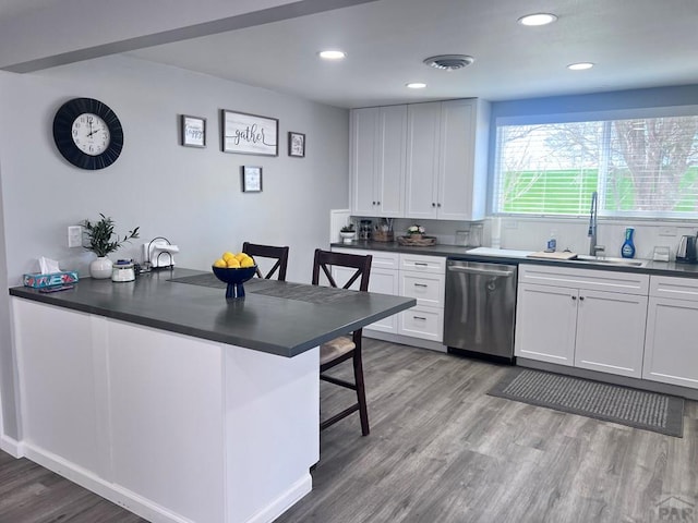 kitchen with dark countertops, visible vents, stainless steel dishwasher, light wood-style floors, and a sink