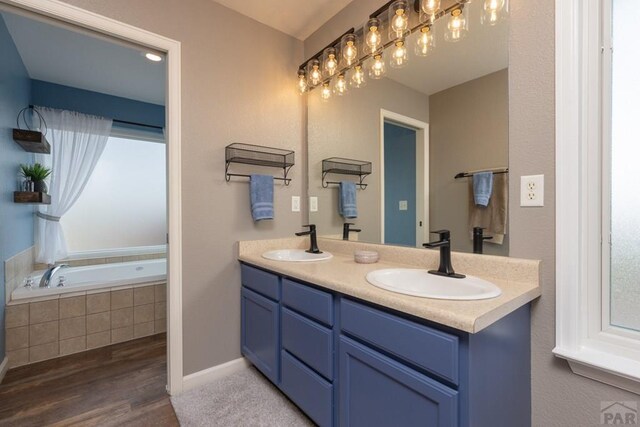 bathroom featuring wood finished floors, a sink, a bath, and double vanity