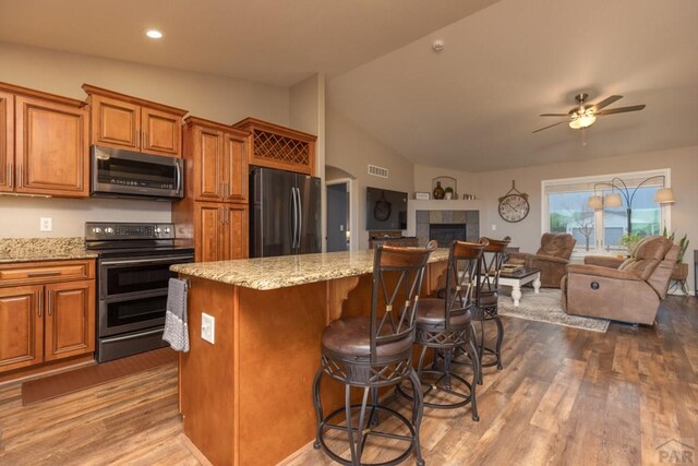 kitchen with open floor plan, appliances with stainless steel finishes, brown cabinets, and a kitchen breakfast bar