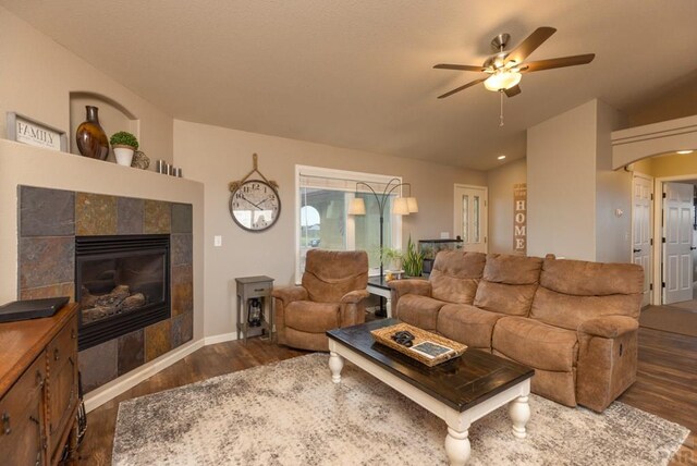 living area with lofted ceiling, a tiled fireplace, dark wood-style floors, and a ceiling fan