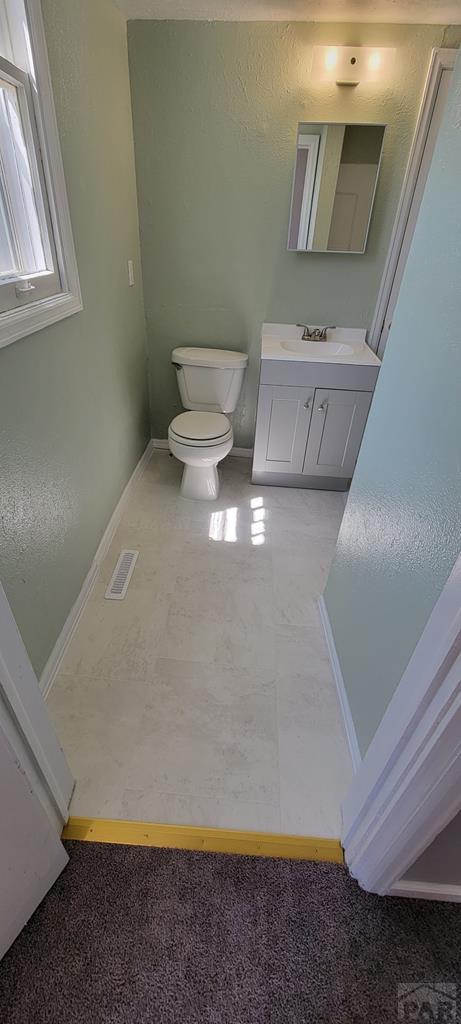 605 E 8th St, La Junta, CO 81050 - bathroom featuring vanity, toilet, baseboards, and carpet flooring