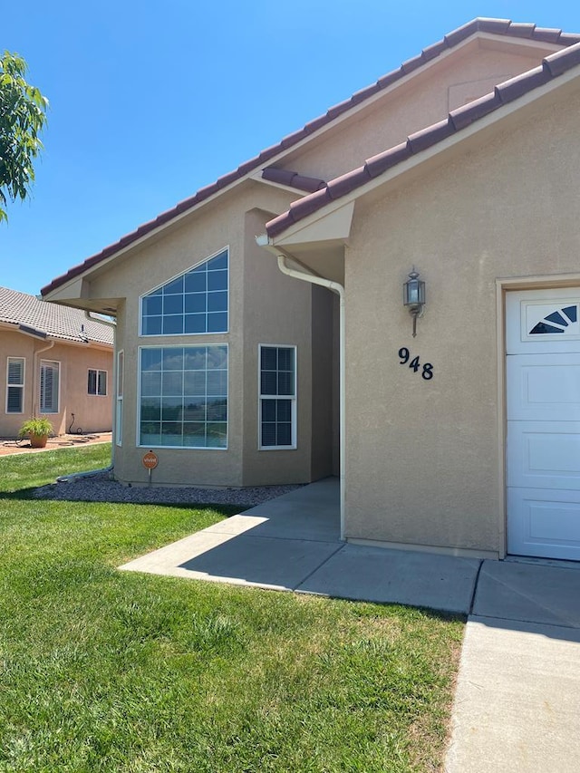 view of exterior entry with an attached garage, a yard, and stucco siding