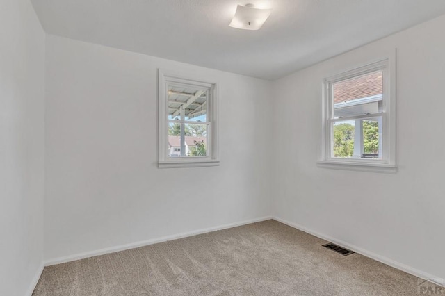 carpeted spare room featuring baseboards, visible vents, and a healthy amount of sunlight