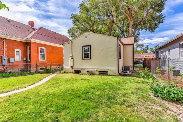 back of house featuring fence, a lawn, and stucco siding