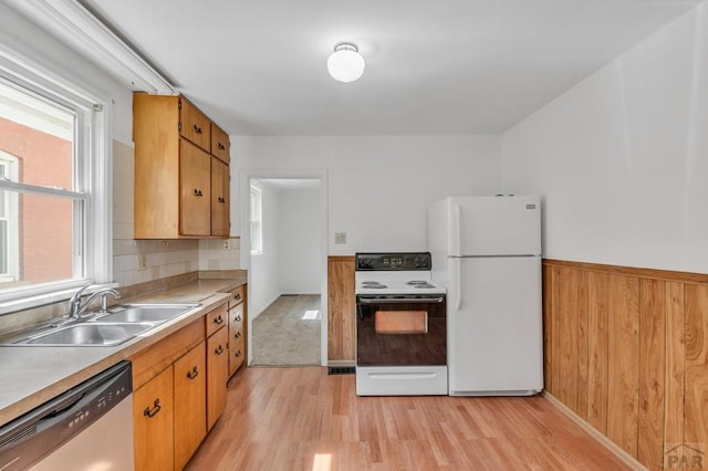 kitchen featuring a wainscoted wall, white appliances, a sink, light countertops, and light wood finished floors