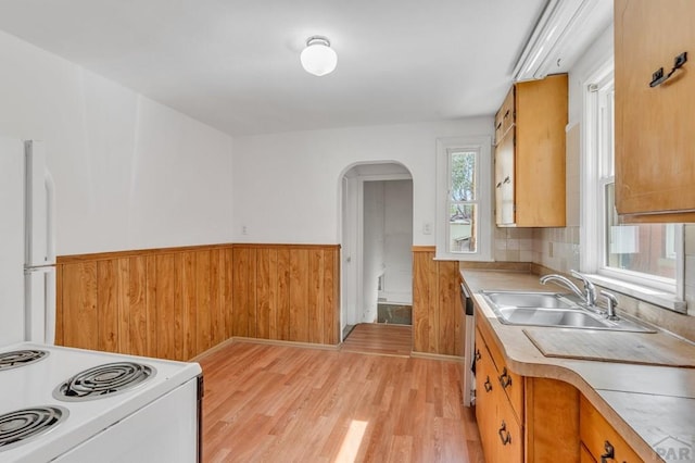 kitchen featuring arched walkways, a wainscoted wall, white appliances, a sink, and light countertops