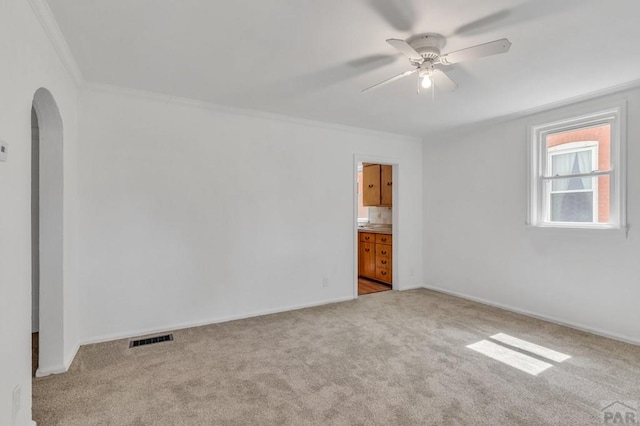 empty room featuring arched walkways, light colored carpet, visible vents, ornamental molding, and a ceiling fan