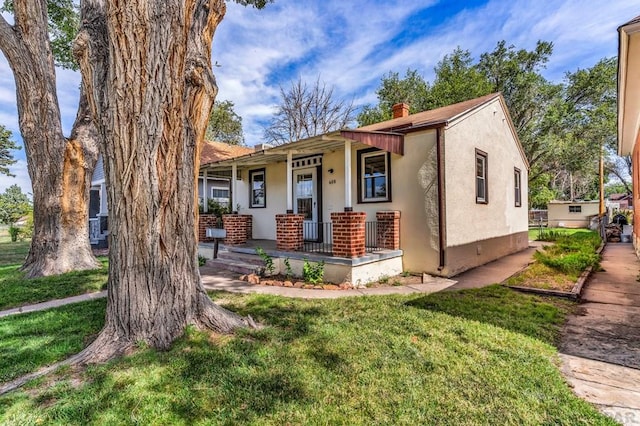 view of front of property featuring covered porch, a chimney, a front lawn, and stucco siding