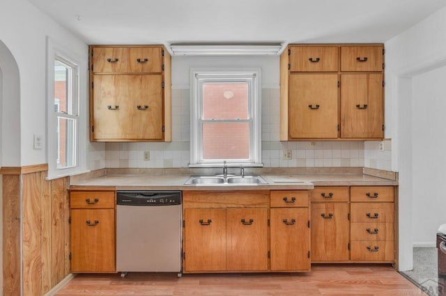 kitchen featuring light countertops, light wood-style flooring, decorative backsplash, a sink, and dishwasher