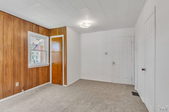 spare room featuring light carpet, wooden walls, and visible vents