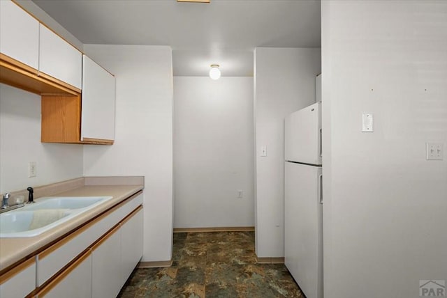 kitchen with a sink, white cabinetry, light countertops, freestanding refrigerator, and stone finish flooring