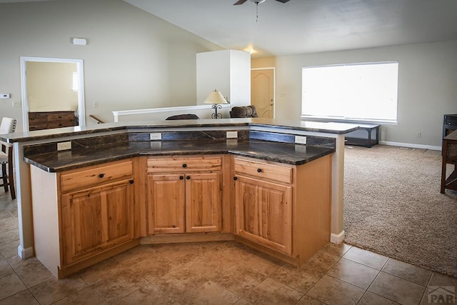 kitchen featuring brown cabinets, open floor plan, light colored carpet, and dark stone countertops