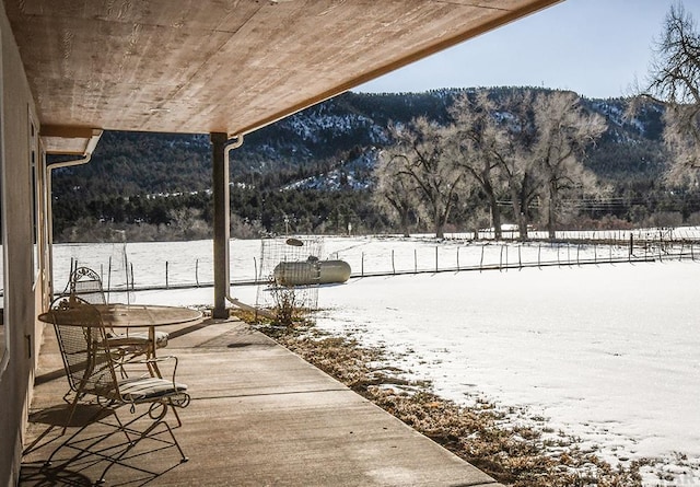 snow covered patio with a mountain view and fence