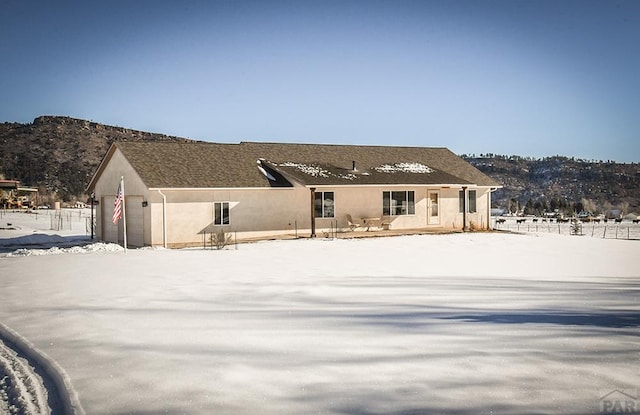 snow covered rear of property featuring a garage, a mountain view, and stucco siding