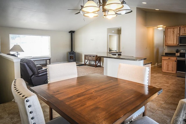 dining area featuring light tile patterned floors, a ceiling fan, a wood stove, vaulted ceiling, and baseboards