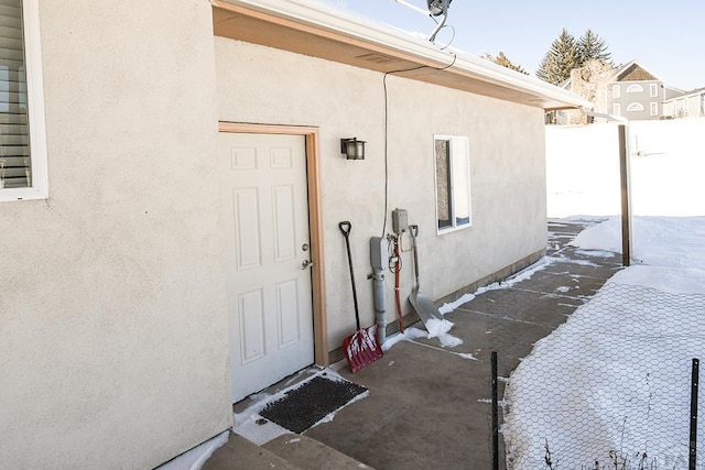 snow covered property entrance with fence and stucco siding