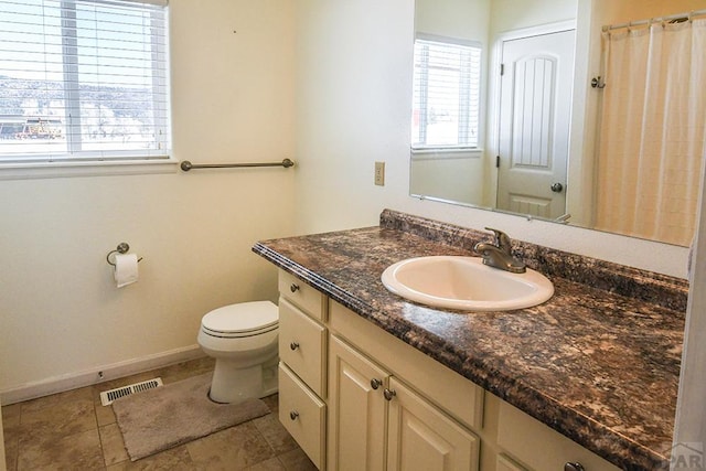 bathroom with toilet, vanity, visible vents, and baseboards