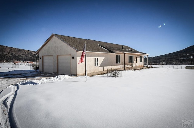 snow covered rear of property with a garage and stucco siding