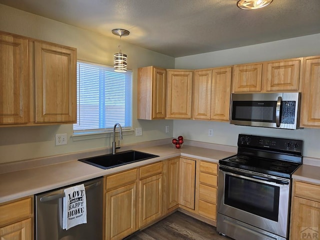 kitchen featuring appliances with stainless steel finishes, light countertops, a sink, and light brown cabinetry