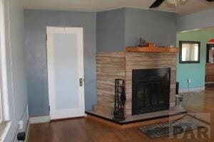 living room with ceiling fan, baseboards, a fireplace with raised hearth, and wood finished floors