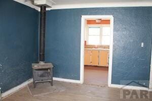 unfurnished living room featuring a wood stove, baseboards, and wood finished floors