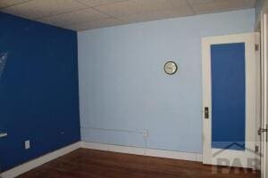 spare room featuring dark wood finished floors, a paneled ceiling, and baseboards