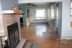 unfurnished living room featuring a fireplace with raised hearth, dark wood-style flooring, a ceiling fan, and baseboards