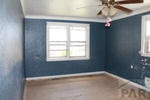 spare room featuring baseboards, ornamental molding, a ceiling fan, and wood finished floors