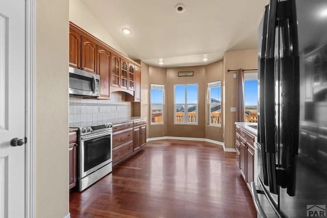 kitchen with light countertops, appliances with stainless steel finishes, backsplash, brown cabinets, and glass insert cabinets