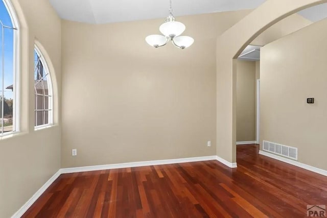 unfurnished dining area featuring dark wood-style floors, arched walkways, visible vents, and baseboards