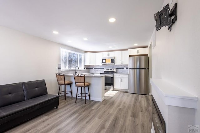 kitchen with stainless steel appliances, a peninsula, white cabinetry, a kitchen breakfast bar, and tasteful backsplash