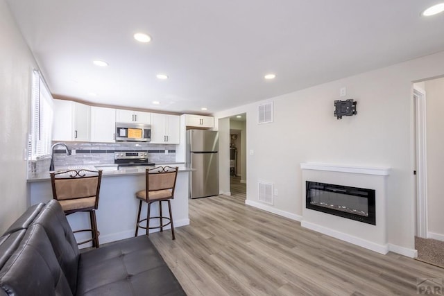 kitchen featuring open floor plan, stainless steel appliances, visible vents, and white cabinets