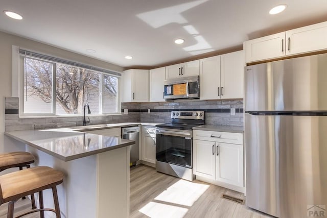 kitchen featuring white cabinets, appliances with stainless steel finishes, a breakfast bar area, a peninsula, and a sink