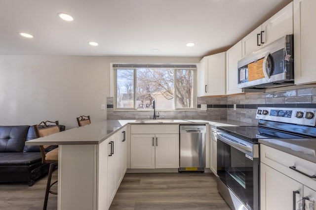 kitchen with stainless steel appliances, a peninsula, white cabinets, a kitchen breakfast bar, and backsplash