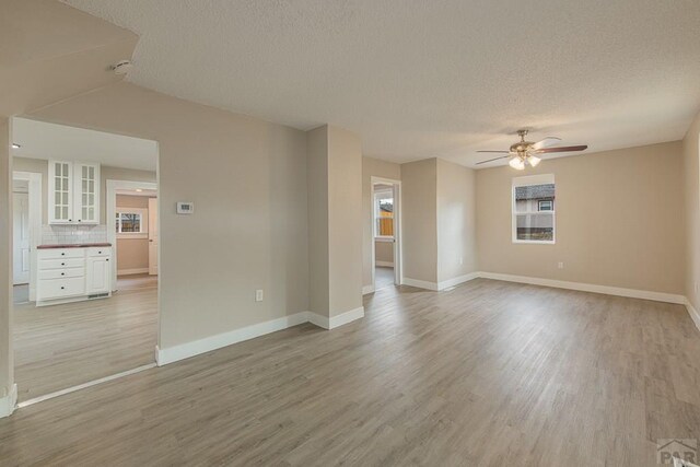 unfurnished room with a textured ceiling, light wood finished floors, a ceiling fan, and baseboards