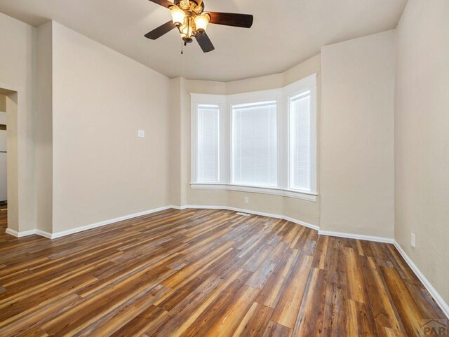 spare room with dark wood-style floors, ceiling fan, and baseboards