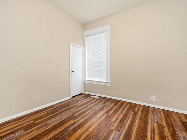 spare room with dark wood-style floors, visible vents, and baseboards