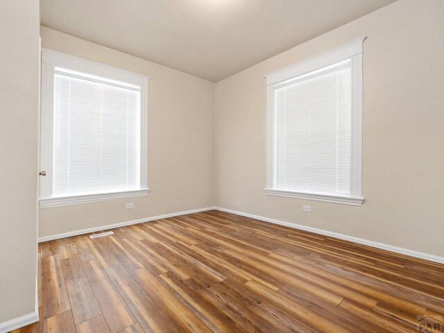 unfurnished room featuring wood finished floors, visible vents, and baseboards