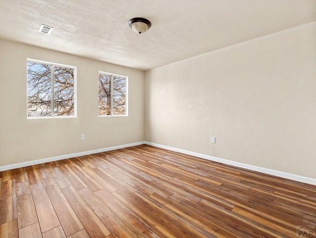 unfurnished room featuring baseboards, a textured ceiling, visible vents, and wood finished floors