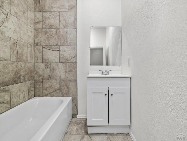 full bath with tub / shower combination, a textured wall, vanity, and baseboards