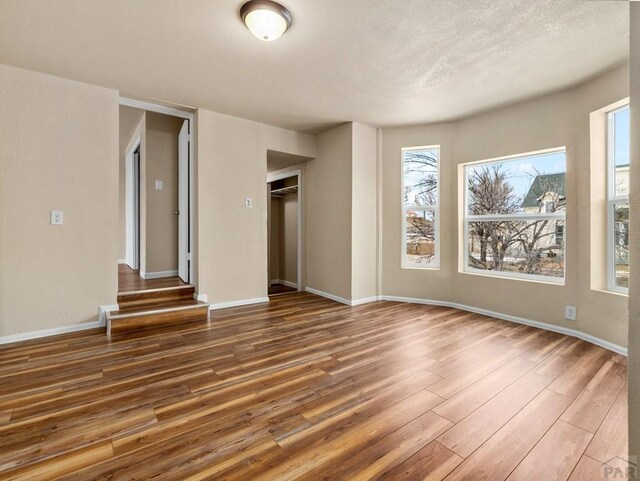 spare room with a textured ceiling, baseboards, and wood finished floors