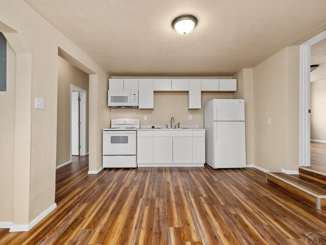 kitchen with white appliances, white cabinetry, light countertops, and dark wood finished floors