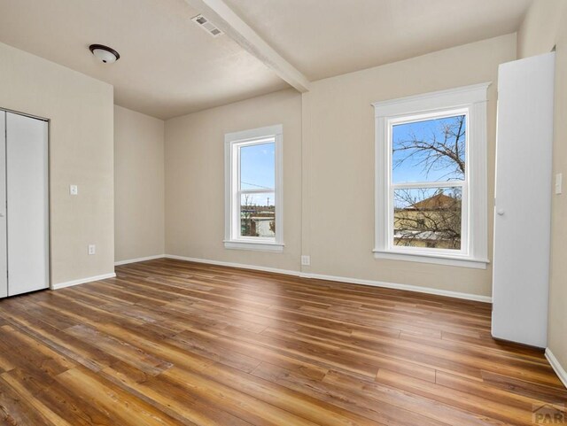 unfurnished bedroom with visible vents, beamed ceiling, baseboards, and wood finished floors