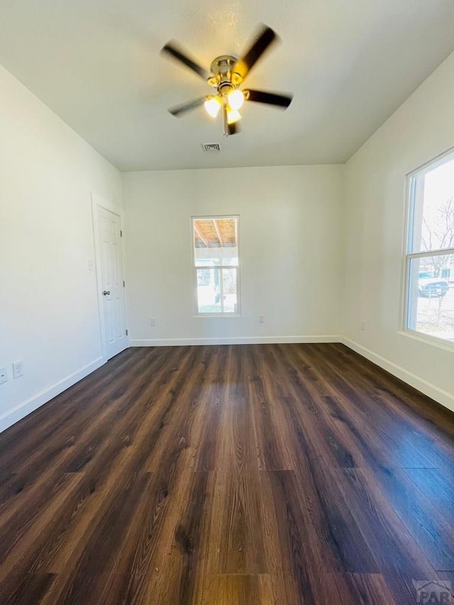 unfurnished room with dark wood-style floors, baseboards, visible vents, and a ceiling fan