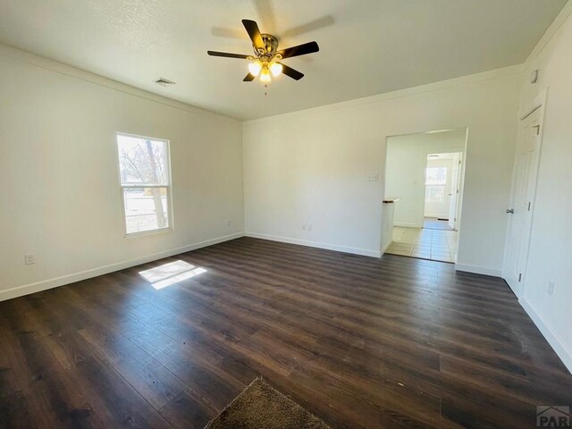 spare room with dark wood finished floors, visible vents, ornamental molding, ceiling fan, and baseboards