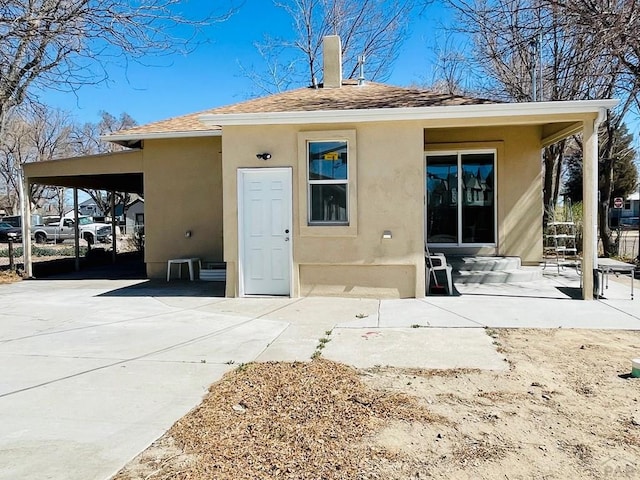 back of house with entry steps, a shingled roof, concrete driveway, an attached carport, and stucco siding